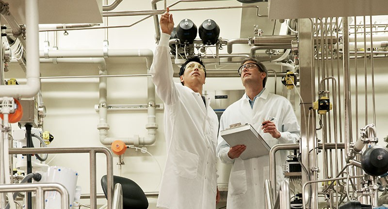 两个穿着白大褂的男科学家指着天花板，手里拿着笔记本。