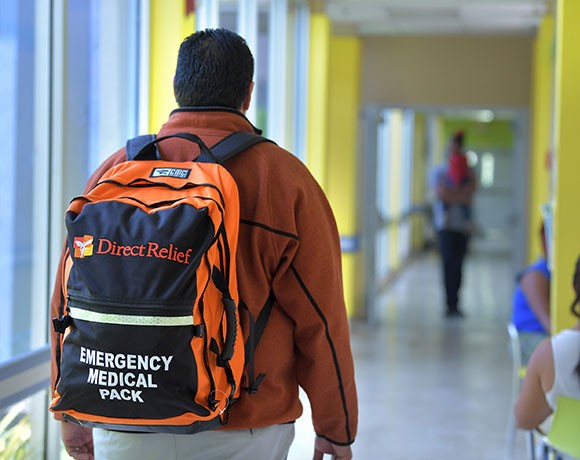 一个人走过一条走廊戴着背包，说“直接救济，紧急医疗包”